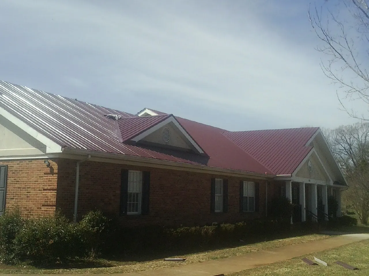 Red metal roof with gabled entries on a long brick building, from a Hail Damage Roof Repair job in Newfoundland