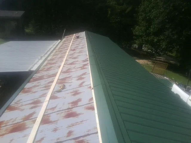 Old rusted panels beside newly installed green metal roofing — Wind Damage Roof Repair by Roofing Brothers in Newfoundland